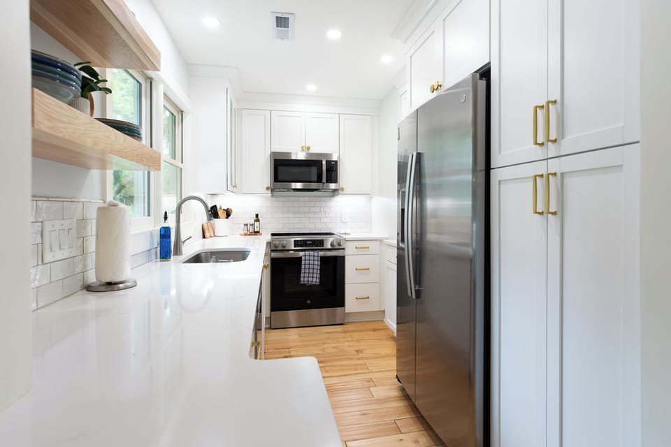 The bright, fully equipped galley kitchen features sleek quartz countertops, open wooden shelving, and high-quality stainless-steel appliances.