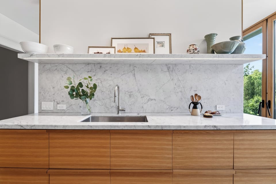 High-end marble backsplashes and floating open shelves bring a sophisticated, modern texture to the kitchen counter.