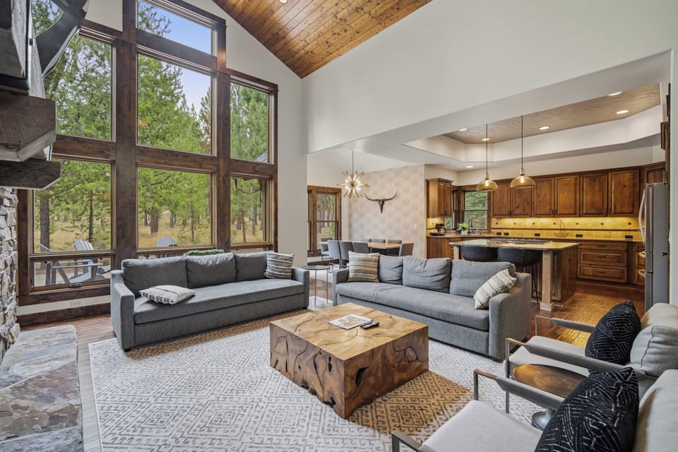 Relax into your mountain retreat where soaring ceilings meet warm wood tones and towering windows frame the forest outside. Sink into plush sofas, gather around the sculptural coffee table, and let natural light pour in while you unwind.