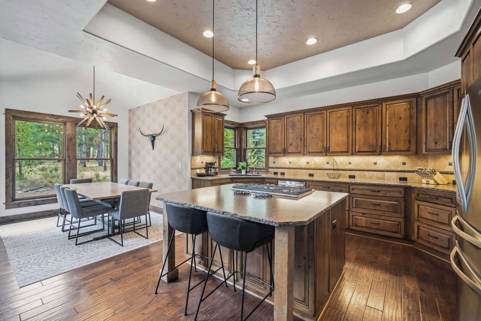 Gather around the large island in your fully equipped gourmet kitchen, where rustic wood cabinetry and modern appliances meet mountain views through elegant windows—perfect for preparing meals and creating memories together.