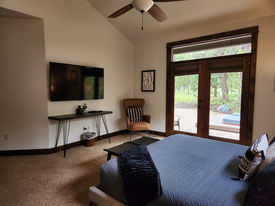 Wake up to peaceful forest views from your cozy bedroom, featuring a plush bed, modern entertainment, and direct access to the outdoors for your morning coffee ritual.