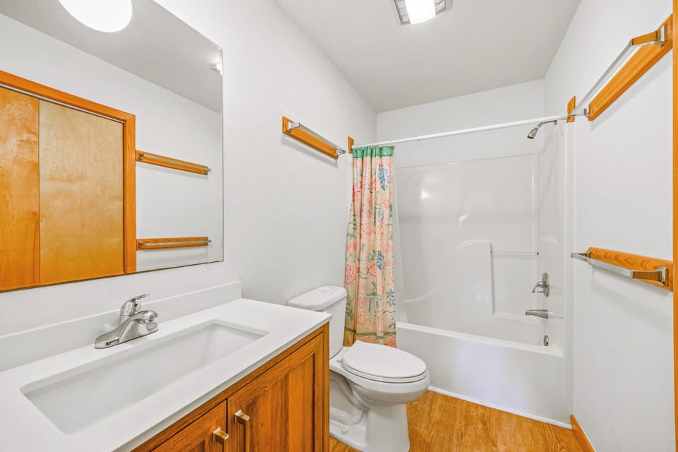 A clean, functional bathroom with a tub-shower combo, warm wood accents, and plenty of towel racks to keep your essentials organized and within reach.