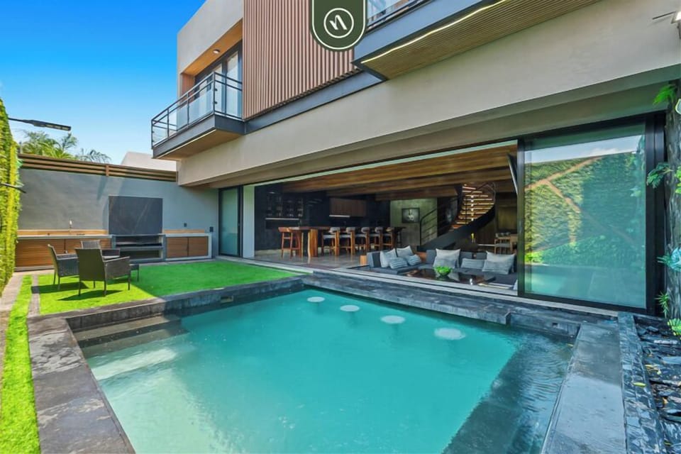 Stunning private pool with a sleek modern design, surrounded by lush greenery and a spacious patio. Enjoy seamless indoor-outdoor living with open seating, a bar area, and a tranquil space perfect for relaxing or entertaining.