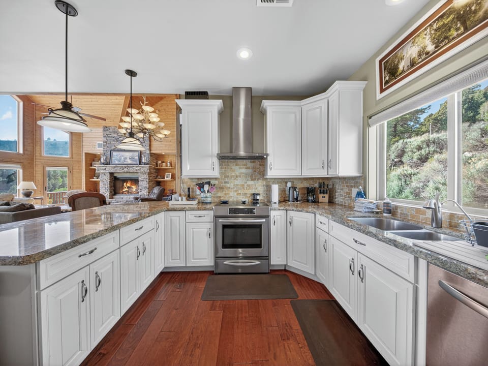 Your bright gourmet kitchen flows into a warm living space with a stone fireplace and windows framing natural vistas, perfect for gathering and creating vacation memories.