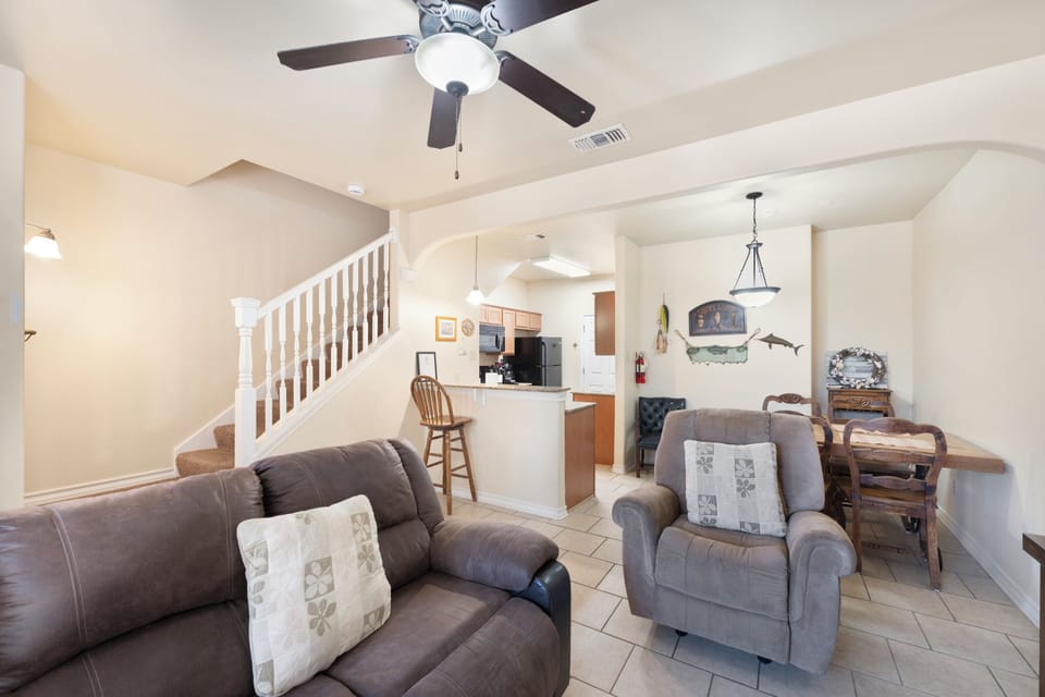 Settle into your open-concept living area with plush seating, ceiling fan, and tile flooring. The kitchen and dining space flow seamlessly, making your stay feel like home.