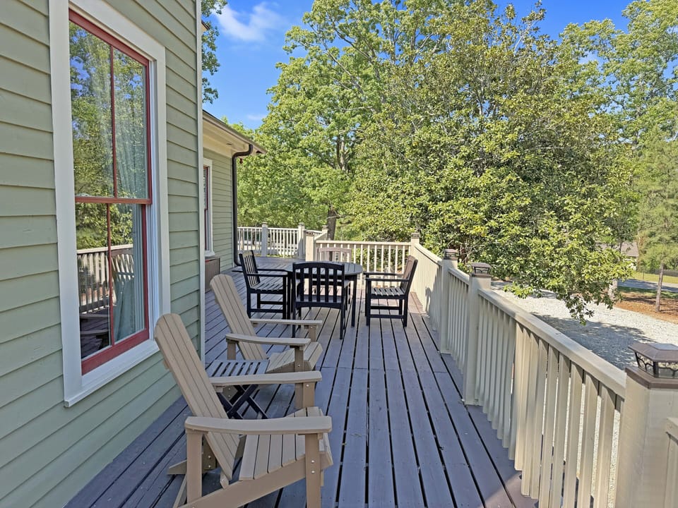 Spacious tree-lined deck with Adirondack chairs and dining set