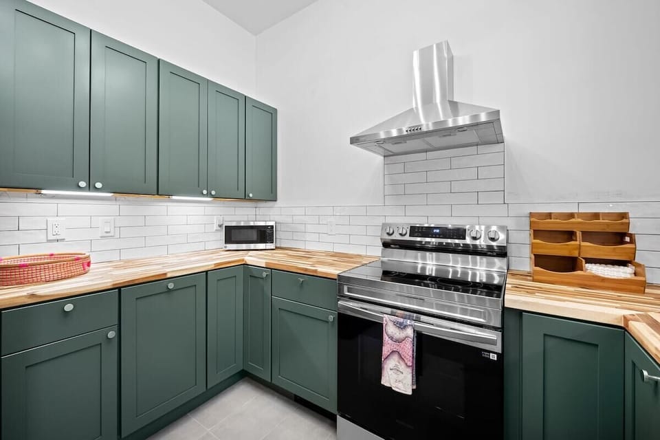 Stylish kitchen with green cabinetry, butcher block counters & stainless appliances
