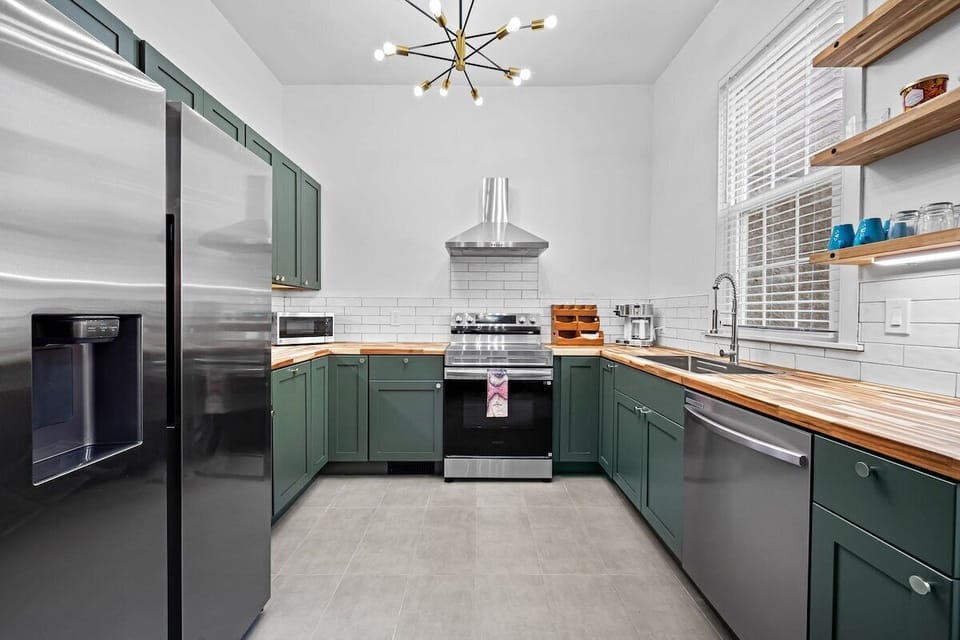 Bright modern kitchen with green cabinets, butcher block counters, and stainless steel