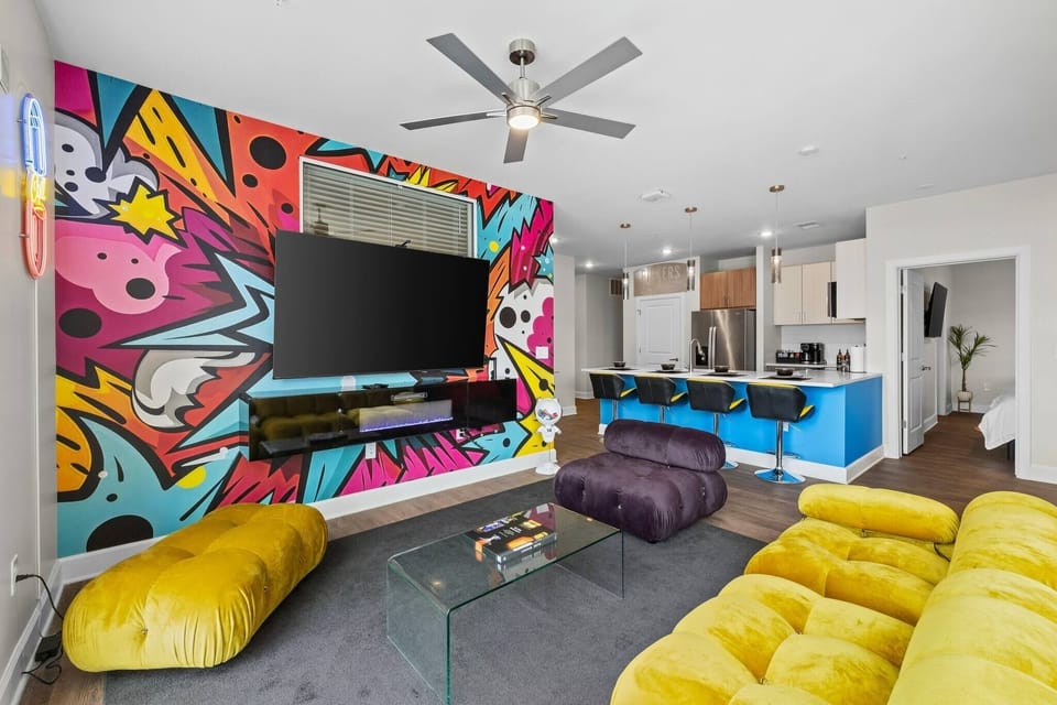 - Colorful living room with bold mural and comfy seating 
- Large TV and vibrant design for entertainment nights 
- Open-concept layout perfect for fun group getaways 