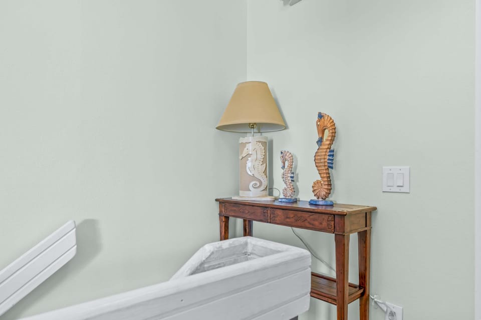 Bedroom Corner Detail: A carved wood console holds a seahorse-printed lamp and a pair of painted seahorse figurines, an easy nod to the shoreline just outside.