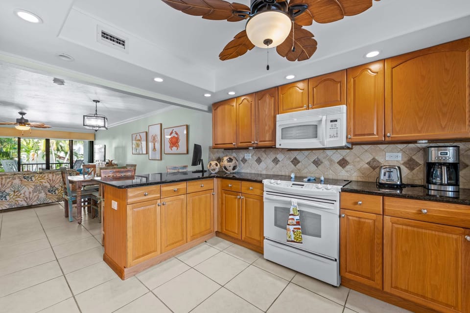 Kitchen: Warm oak cabinetry meets dark granite counters and a tiled backsplash, with a full appliance lineup and coastal artwork that keeps prep work feeling more like vacation than chore.