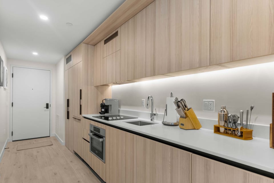 In-Unit Kitchenette: Light wood cabinetry, an induction cooktop, full oven, espresso maker, and full prep tools fit a long galley for everything from morning coffee to a real cooked meal.