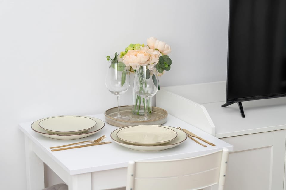 A small dining table set with plates and flowers, arranged beside a window. The bright corner creates an inviting spot for meals.