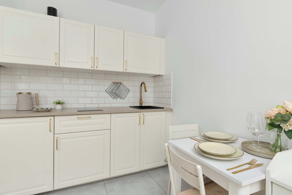 A modern kitchenette with sleek white cabinets, integrated appliances, and a small dining setup. Clean lines emphasize the contemporary design.