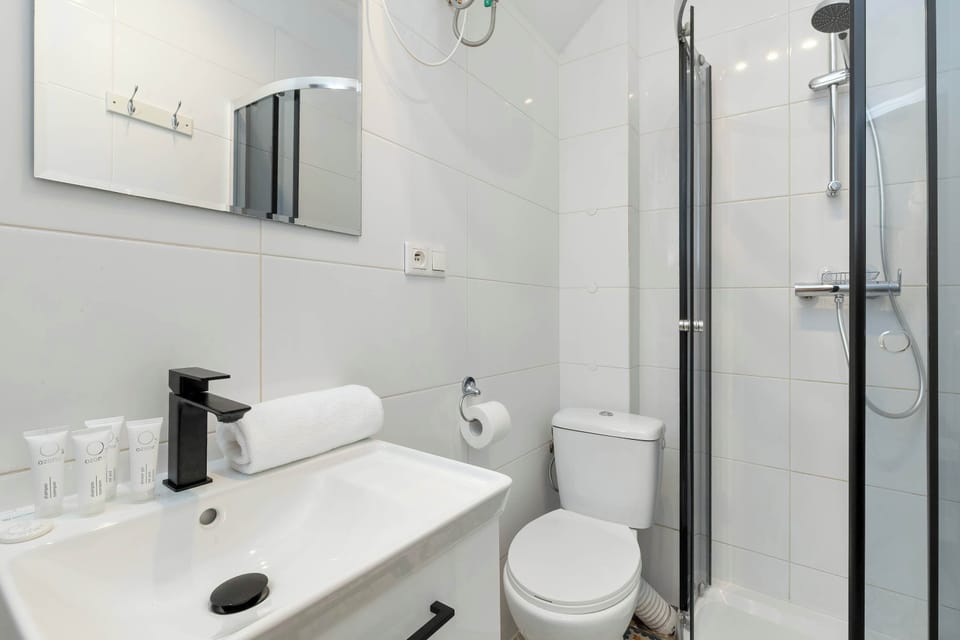 A compact bathroom featuring a vanity sink, glass shower enclosure, and wall-mounted mirror. White finishes make the room appear spacious and fresh.