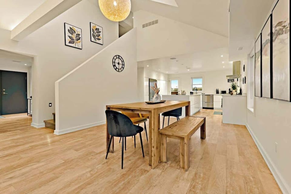 Spacious open-plan dining and kitchen area featuring a solid wooden table, cushioned bench, stylish chairs, decorative wall art, and bright, inviting ambiance.
