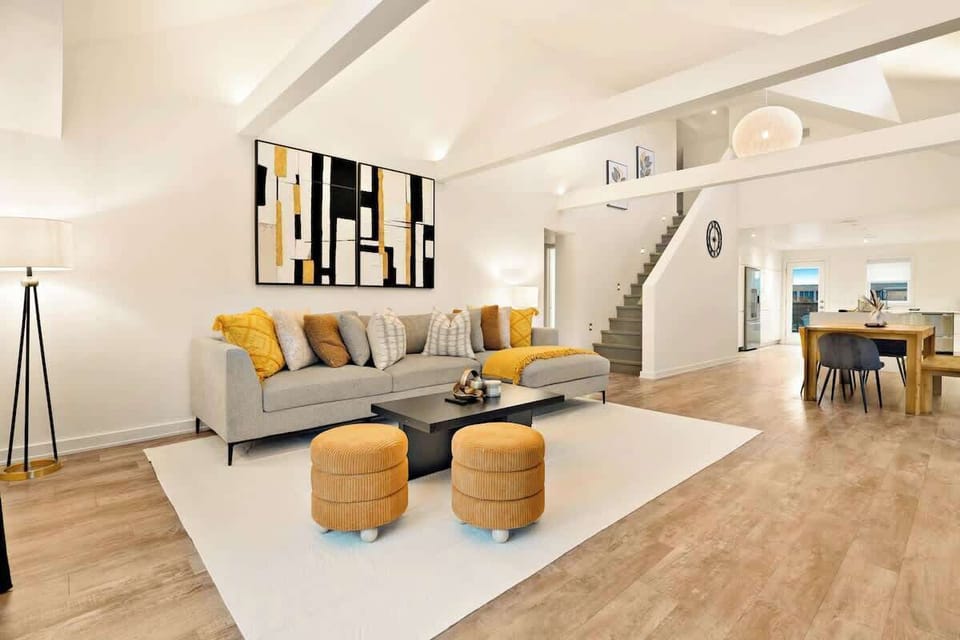 Spacious, stylish living room with plush sectional sofa, cozy poufs, modern coffee table, vibrant artwork, and elegant dining area.