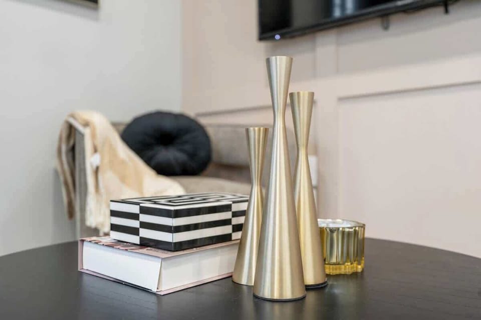 Elegant black coffee table adorned with three sleek metallic vases, a striped decorative box, a hardcover book, and a small amber candle, with a cozy blanket and round pillow on a nearby sofa.