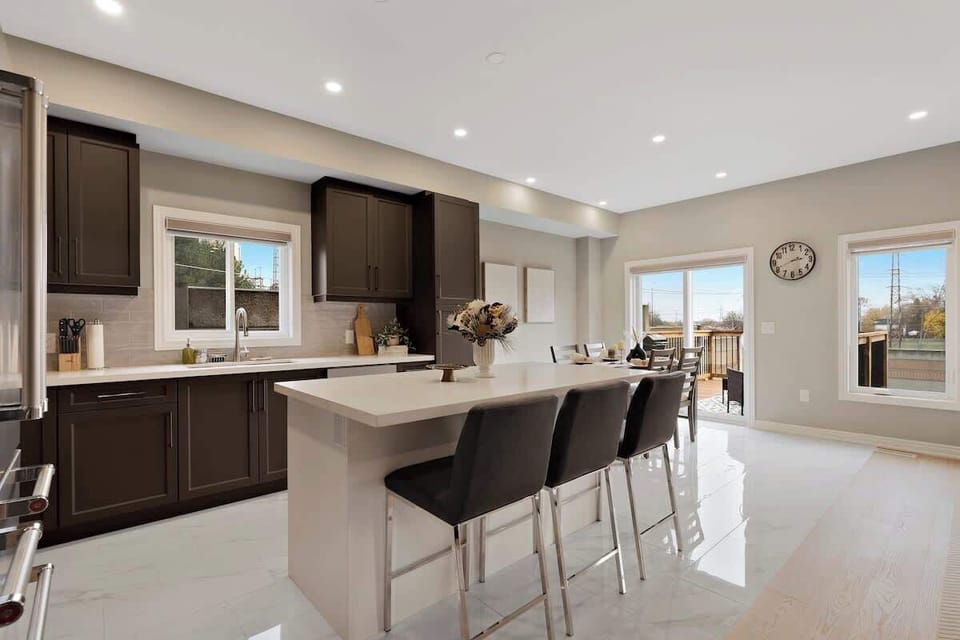 Spacious, bright kitchen with sleek island, comfortable bar stools, modern appliances, elegant cabinetry, large windows, and a cozy dining area with natural light.