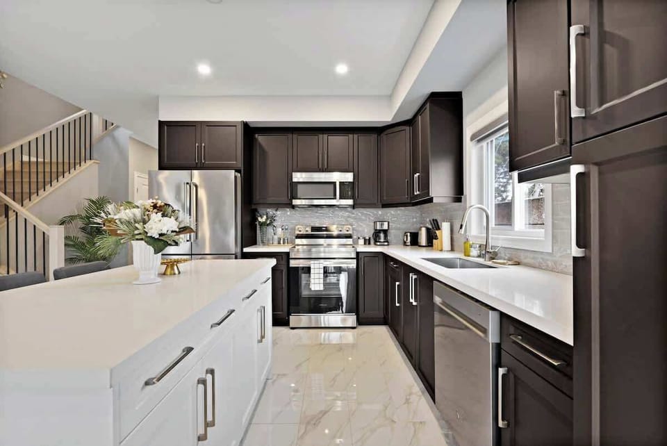 Modern kitchen featuring sleek stainless steel appliances, spacious white island, ample dark cabinetry, polished countertops, elegant marble flooring, and decorative flowers.