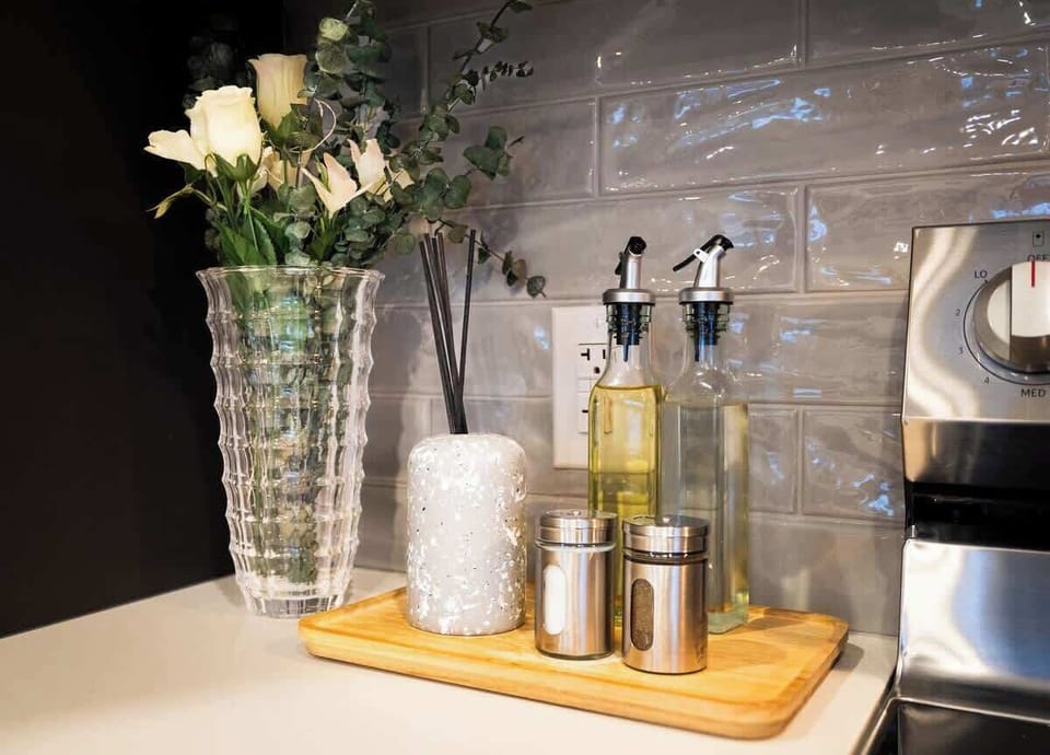 Chic kitchen countertop with elegant glass vase of fresh flowers, scented reed diffuser, olive oil bottles, salt & pepper shakers, all on a wooden tray.