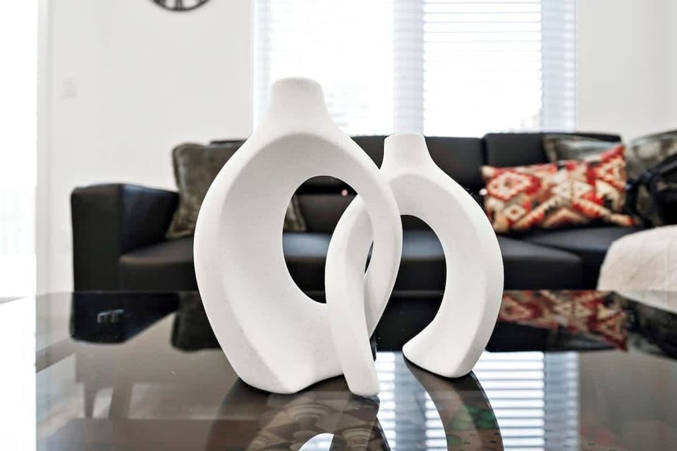 Stylish living area showcasing unique modern ceramic sculptures on a sleek glass coffee table, with plush patterned pillows and a cozy black sofa in the background.