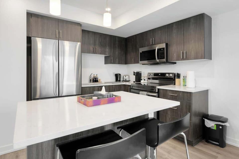 Modern kitchen featuring spacious island with seating, stainless steel fridge, microwave, stove, coffee maker, toaster, sleek cabinetry, and elegant lighting fixtures.
