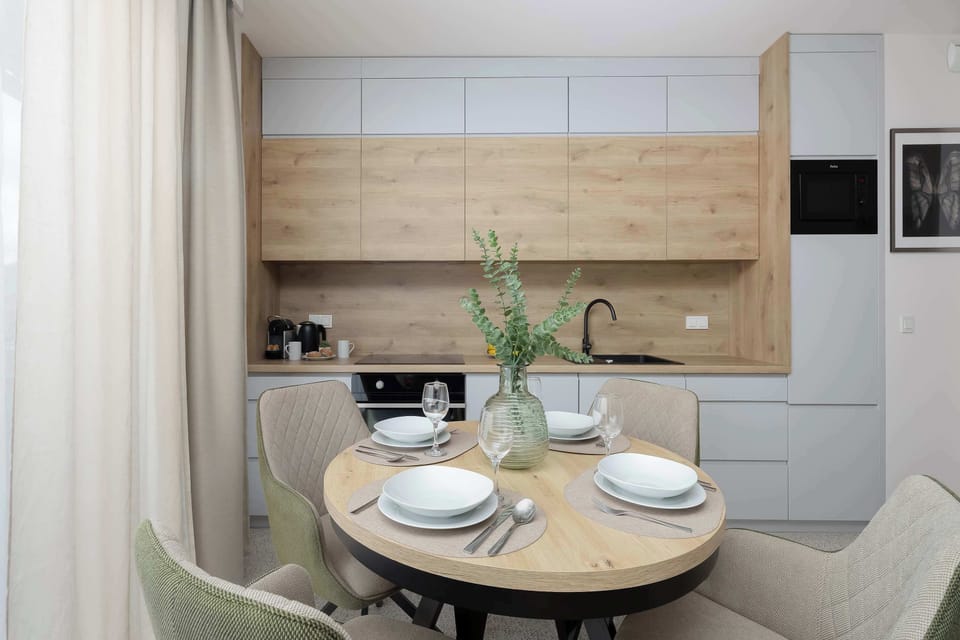 A close-up of the dining table captures the circular wooden surface set for four guests. The kitchen counters in the background remain clean and uncluttered.