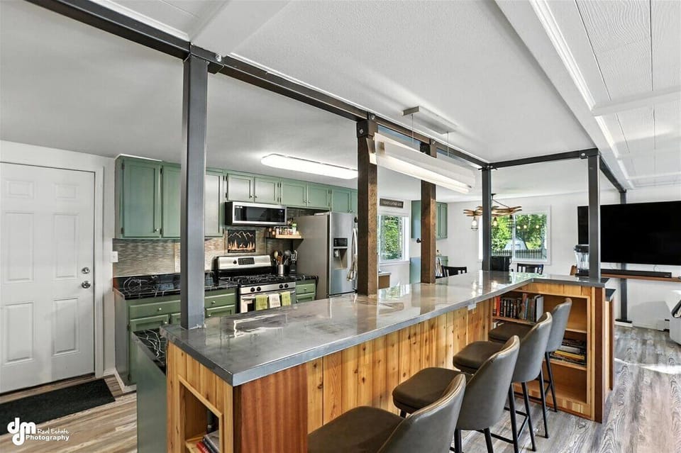 Expansive kitchen with custom cement island bar featuring steel beams and stainless appliances 