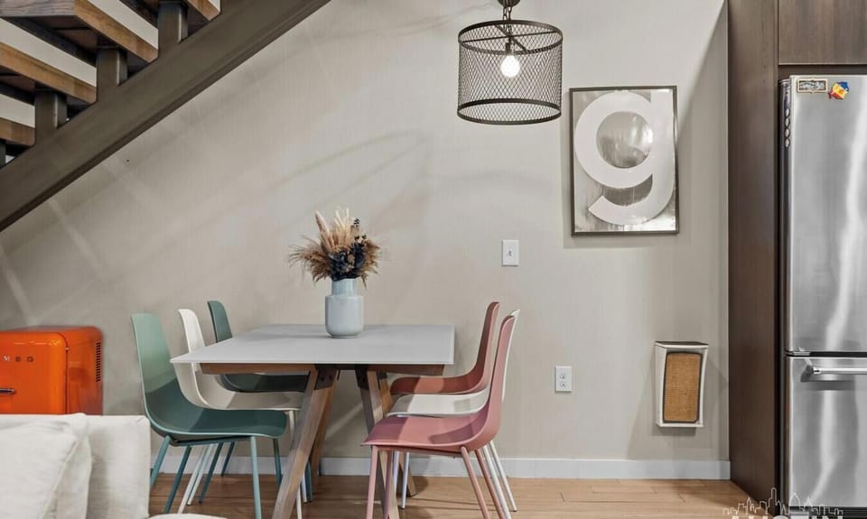 Share meals at the dining nook tucked beneath the staircase, with colorful seating and a fridge close at hand.