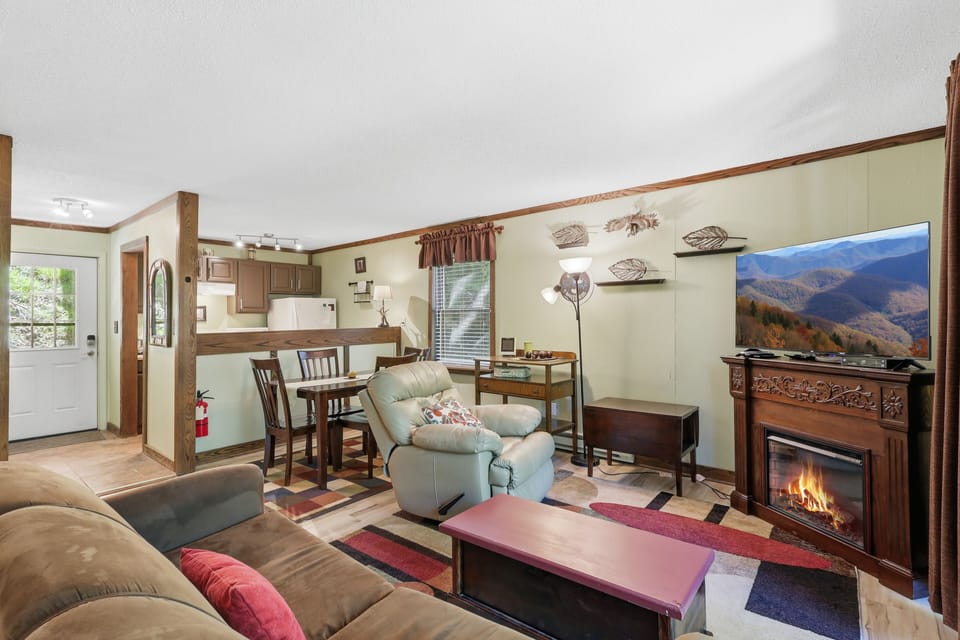 Cozy living room with fireplace, TV, dining nook, and warm cabin charm