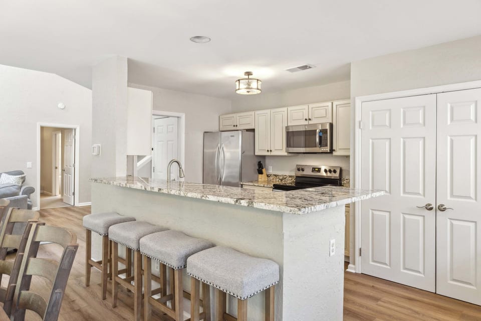 Stone surfaces and cushioned seating invite you to linger over coffee in this open kitchen. Soft hues and modern appliances create a seamless blend of comfort and utility for your morning routine.