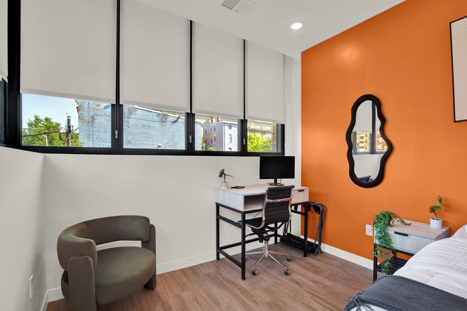 Bright modern bedroom with desk, large windows, and bold accent wall