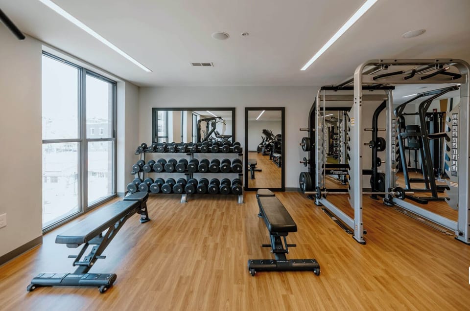 Modern on-site gym with weights, benches, mirrors, and natural light