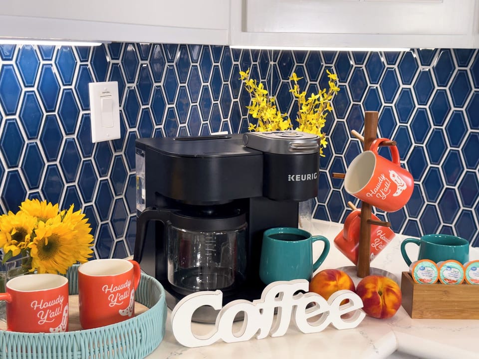 Modern coffee station with coastal décor, coffee maker, and bright kitchen backsplash perfect for enjoying fresh morning coffee.