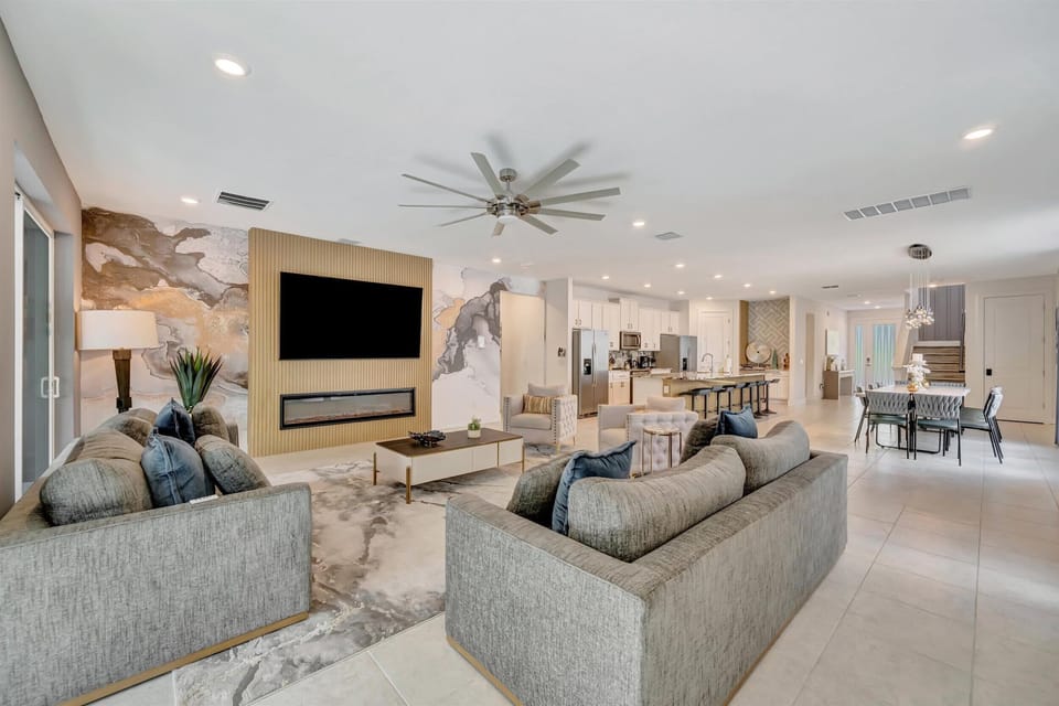 Large living room with plenty of cozy seating, a huge 75+ inch Smart TV, electric fireplace and ceiling fan