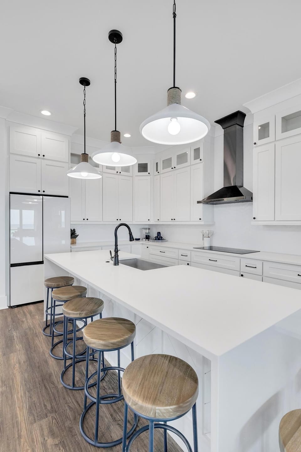 A bright, modern kitchen featuring white cabinetry, sleek pendant lighting, and a spacious island with bar seating—perfect for gathering and meal prep during your stay.