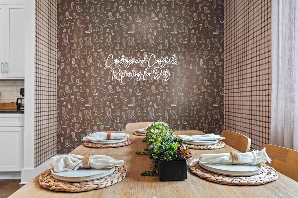 A close-up of the dining room's statement wall — cowboy boot wallpaper, a "Cowboys and Cowgirls Reporting for Duty" neon sign. A photo-worthy moment before every meal.