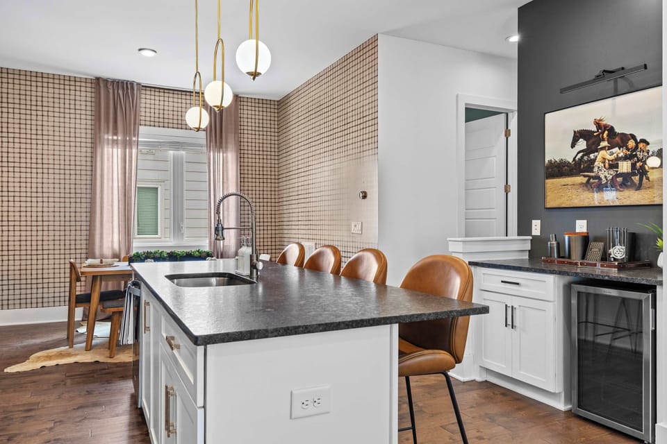 The kitchen and dining areas connect seamlessly, with the island at center, a wine fridge and cocktail bar to one side, and plaid wallpaper wrapping the dining nook. A great layout for group meals.