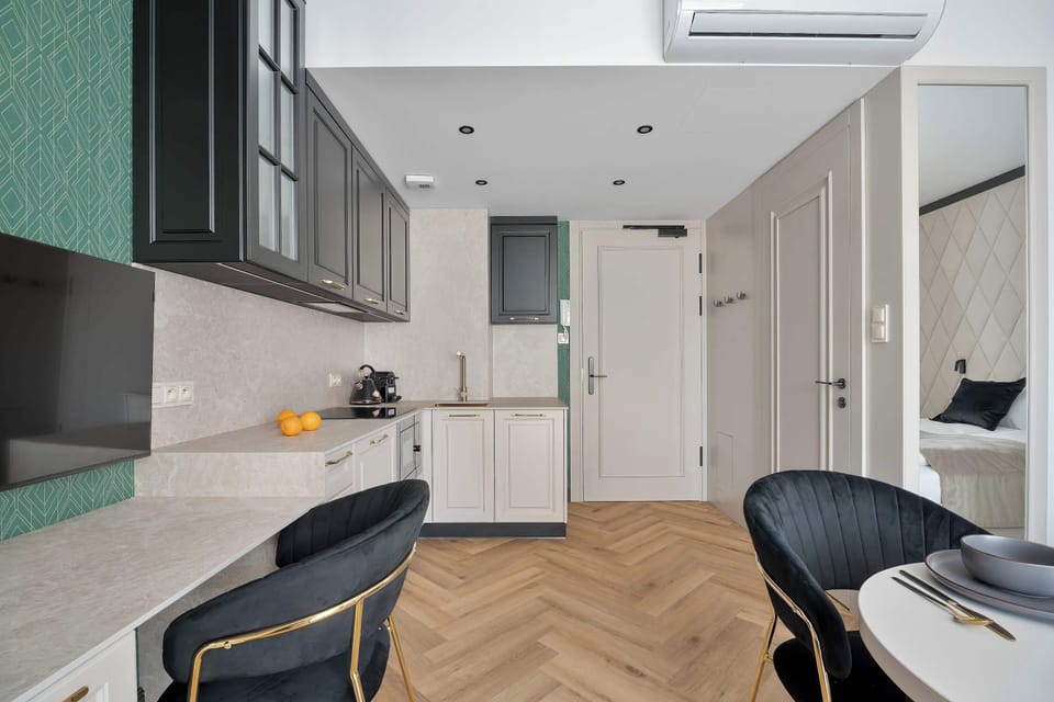A bright hallway leading into a modern apartment with a small workspace setup. Light wood flooring and clean white walls enhance the feeling of openness throughout the space.