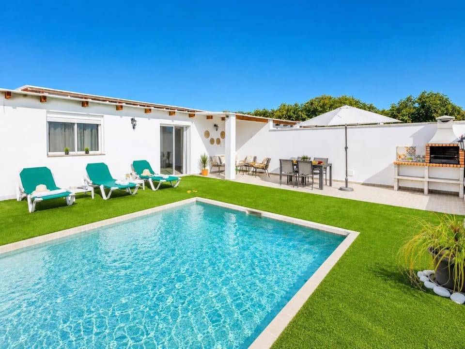 Sunny private pool area with turquoise sun loungers, BBQ dining space, and a bright modern villa setting.