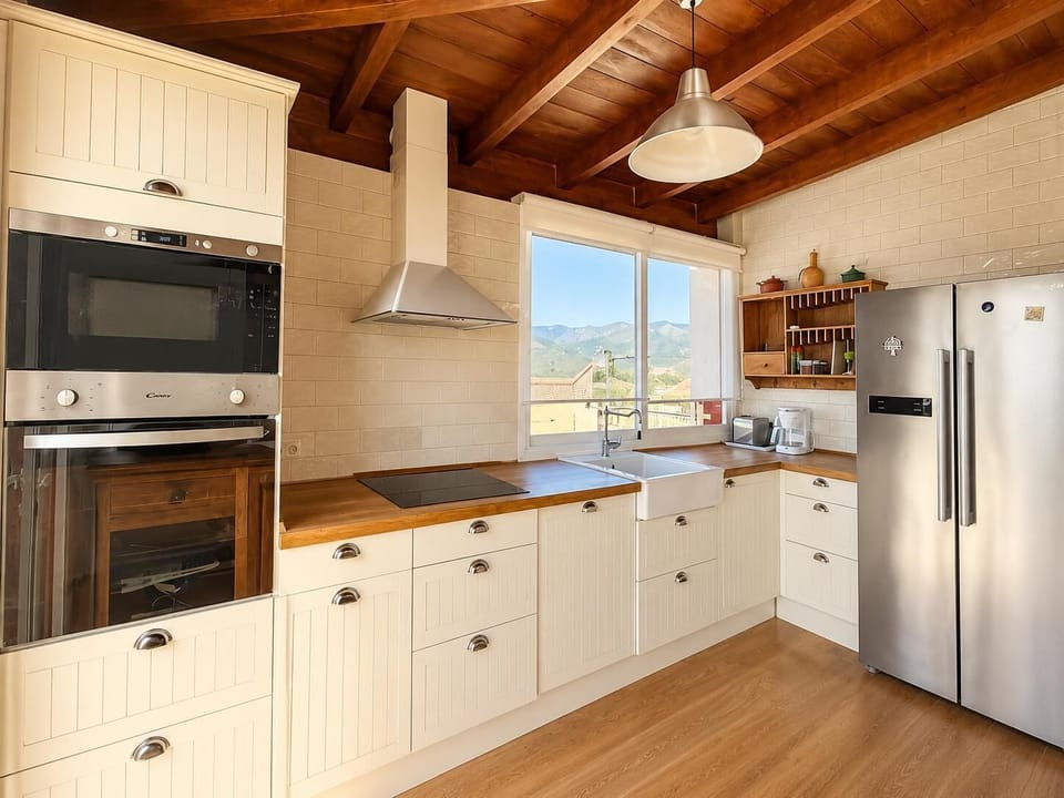 A bright country-style kitchen with wooden ceilings and scenic mountain views.