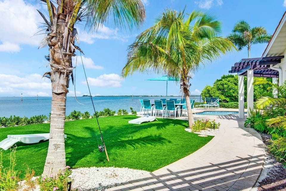Tropical waterfront backyard with palm trees, lawn, and outdoor dining. Fishing paradise