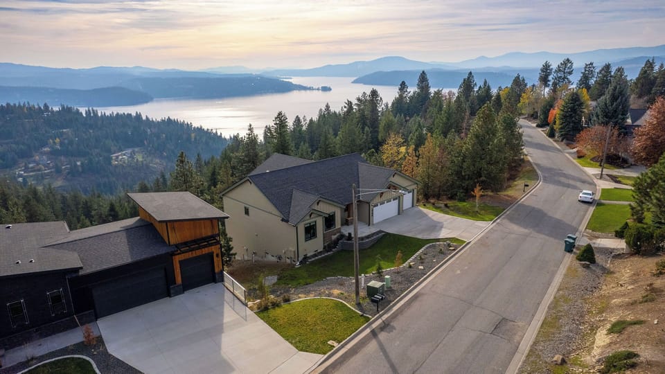Aerial view of a tranquil residential neighborhood nestled among evergreen forests with sweeping lake and mountain vistas in the distance.