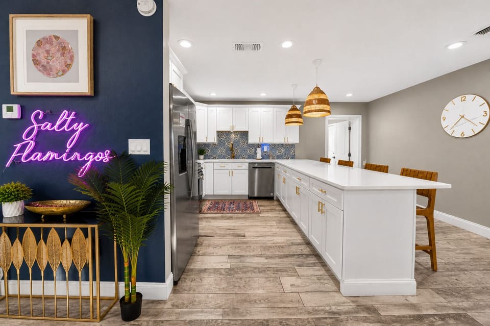 Spacious modern kitchen featuring a large island with bar seating, white cabinetry, and a decorative blue accent wall with a neon "Salty Flamingo" sign.