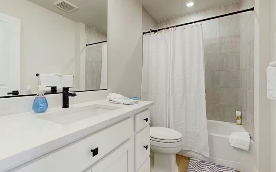 A bright bathroom with a white vanity, modern dark hardware, and a shower-tub combination.