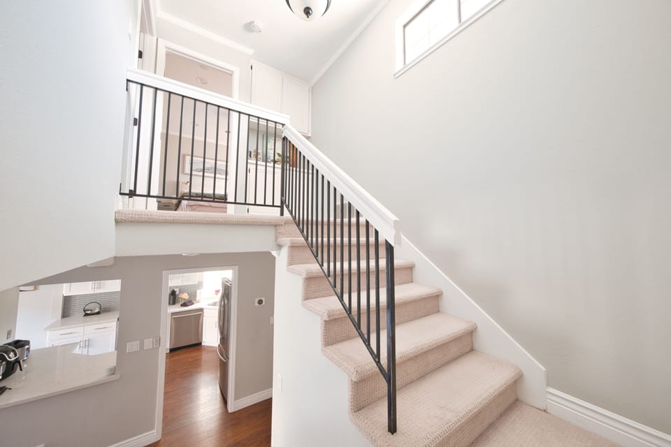 Sunlit stairway with modern railing and view into an updated kitchen