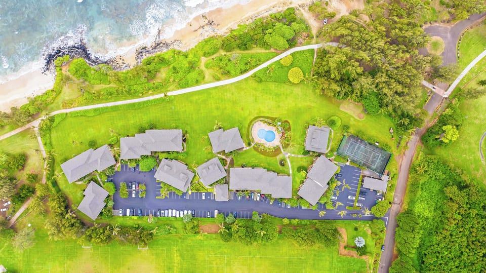 From above green lawns, a curvy pool, and the beach just past the path.