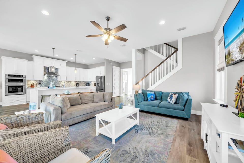 An open great room with coastal blues, a sweeping staircase, and enough seating for every member of the crew — this is where the group lands after a day at the beach.
