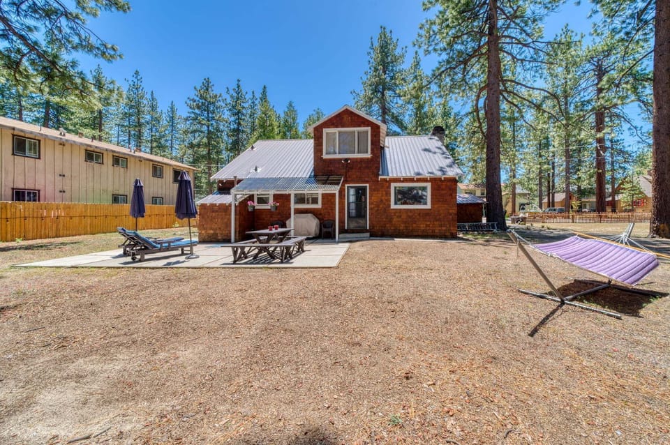 Exterior view featuring trees, patio, umbrella, and picnic table benches.